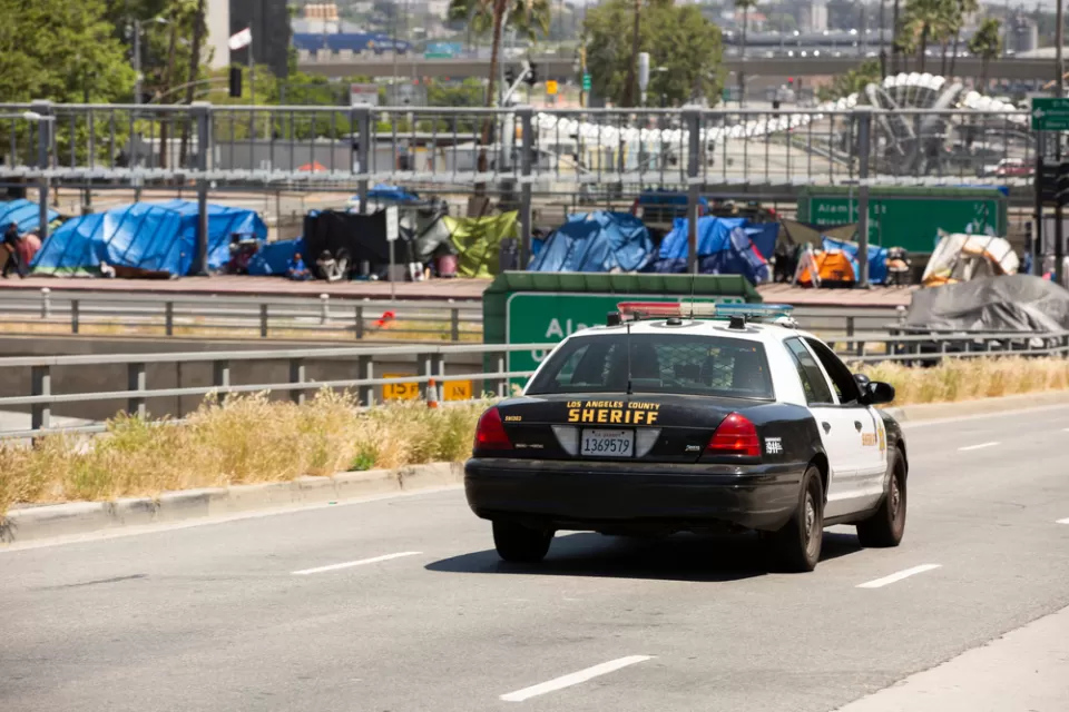 Homeless encampment on overpass in downtown Los Angeles with police car in foreground